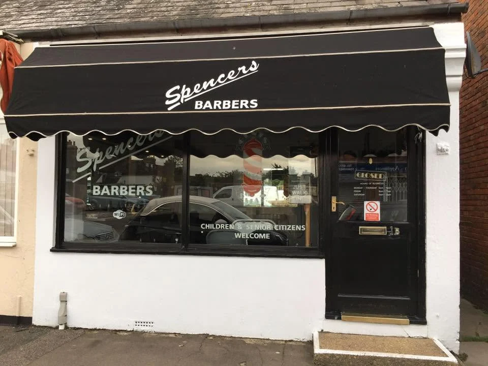 The Spencers Barbers shopfront on Torrington Road: a black scalloped awning with Spencers Barbers in cream lettering, and Children and Senior Citizens Welcome on the window